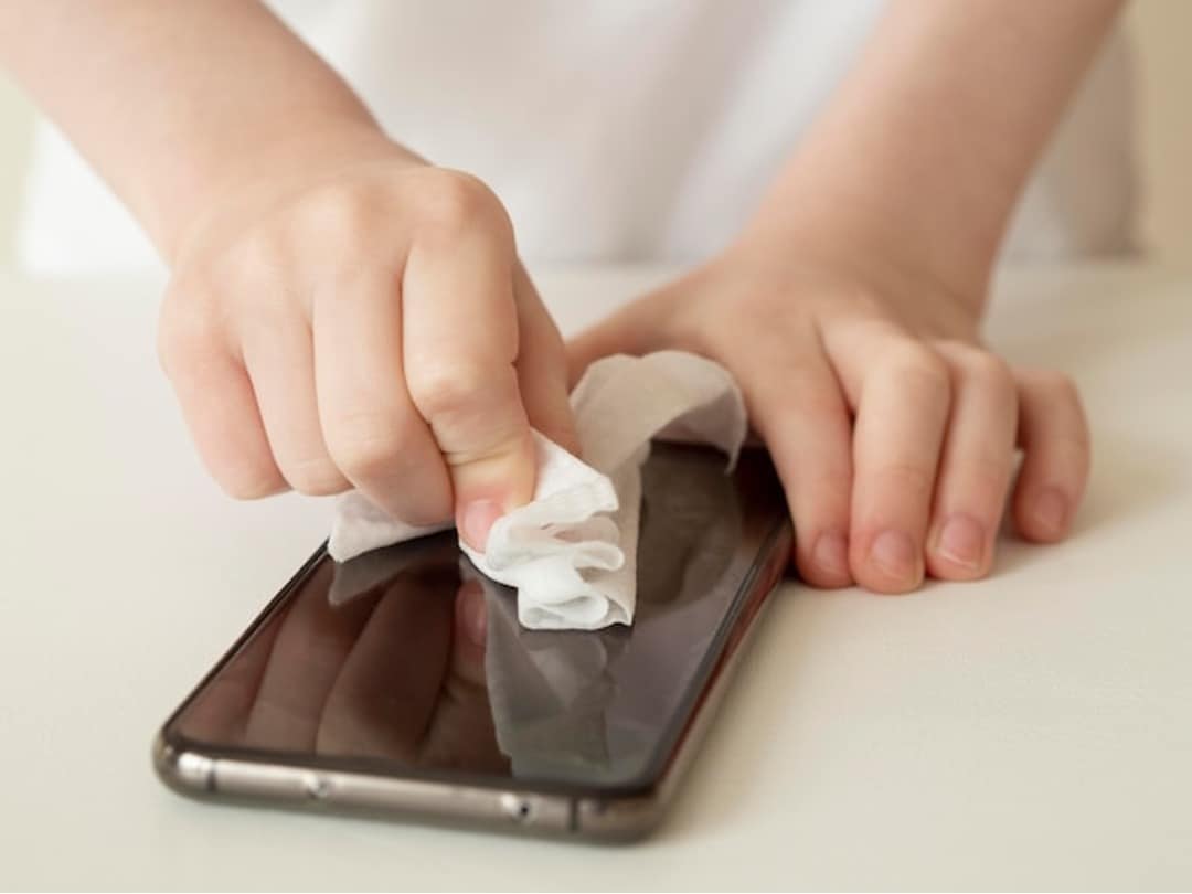 persona limpiando el teléfono con una toalla de papel