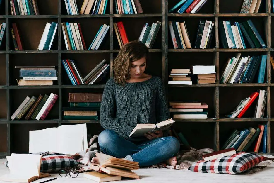 woman reading books beside bookcase