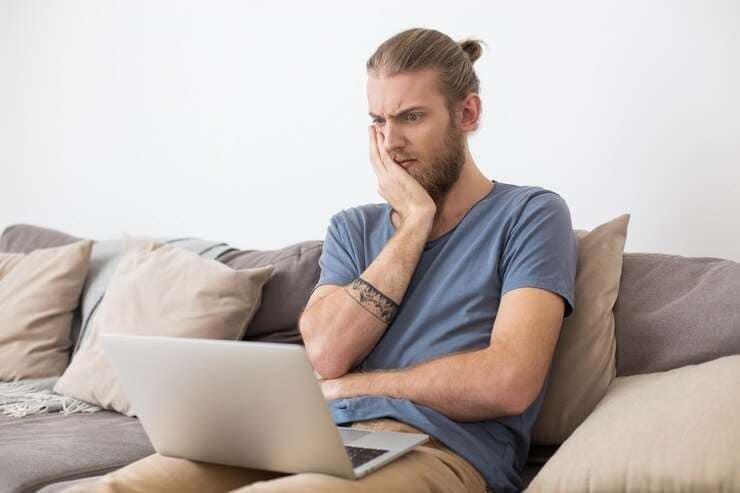 Homem sentado irritado enquanto usa um laptop